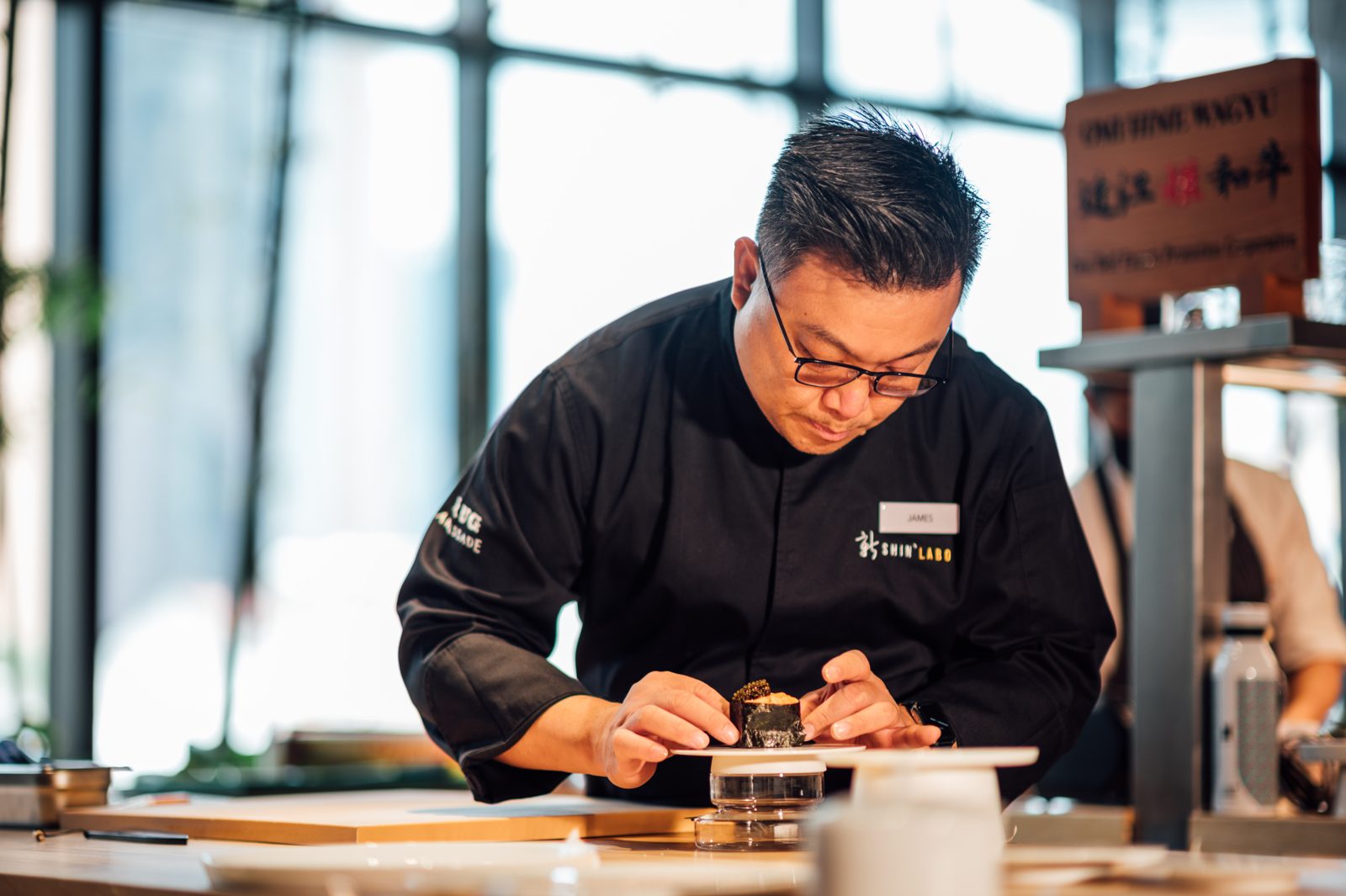 James Won plating at the Shin'Labo counter, in window light.
