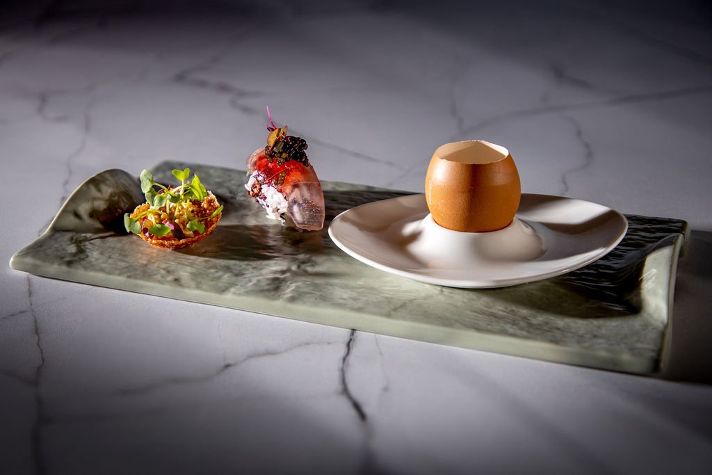 Discover Rarity amuse — Triumphant Trio — Cress Pot scallop chip with herbs, aloe-vera nigiri with caviar, Like The Egg parmesan tofu in eggshell, on a stone slab.