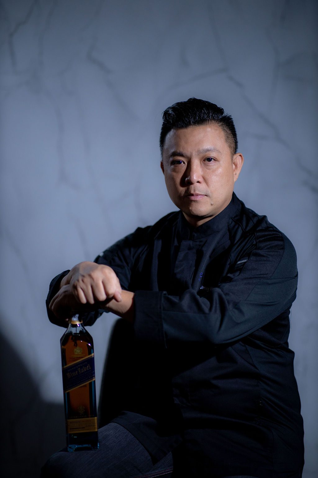 James Won seated in his black Enfin jacket, a bottle of Johnnie Walker Blue Label at his side.
