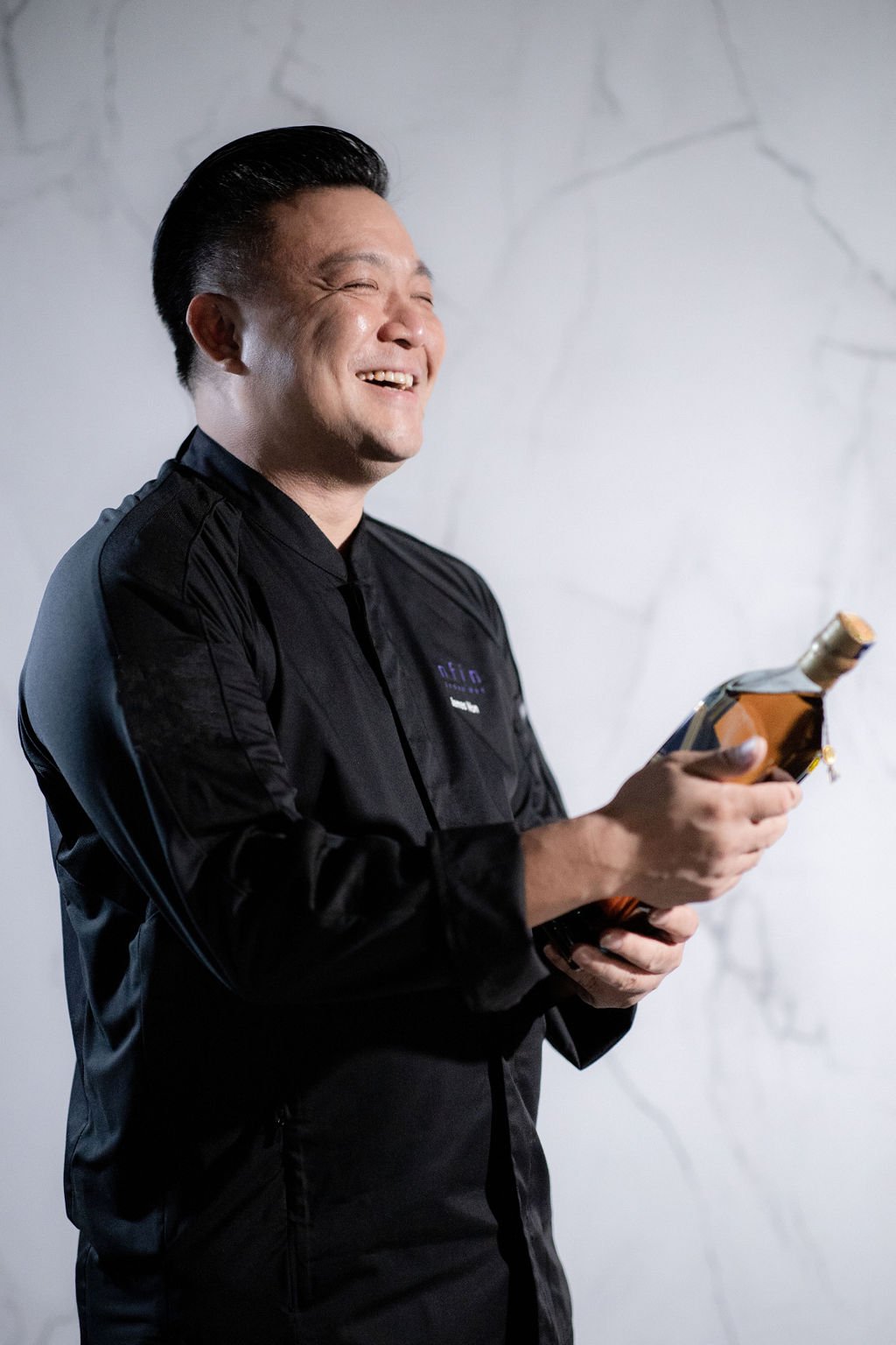 James Won in Enfin black jacket, holding a Johnnie Walker Blue Label bottle, marble wall behind.