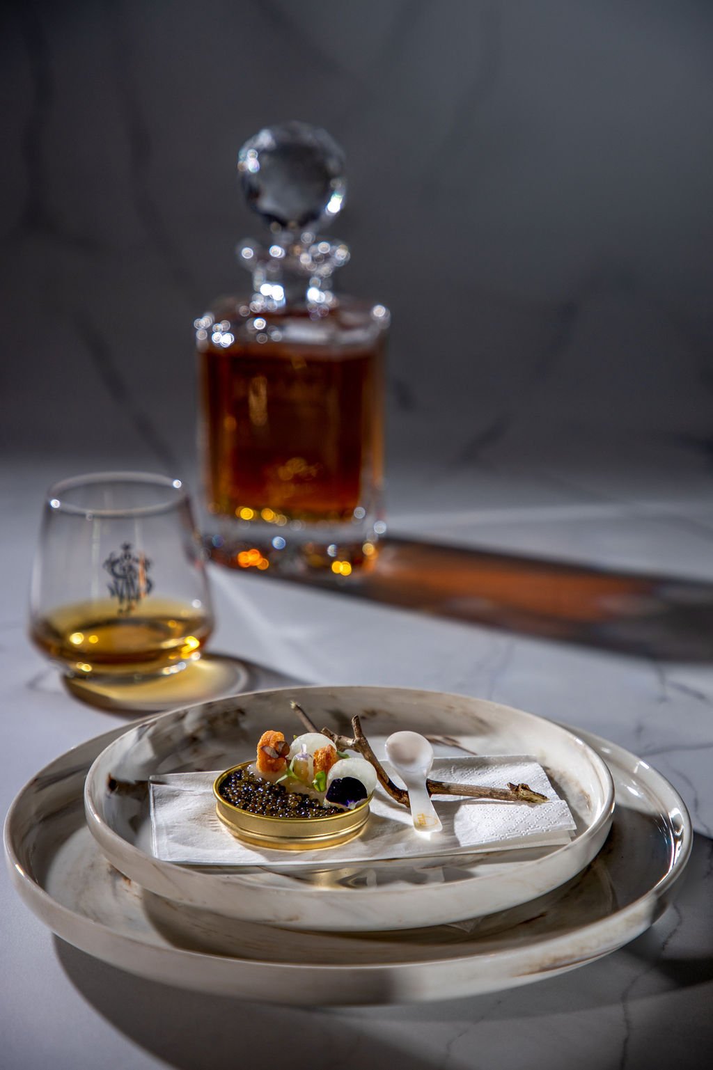 Discover Rarity entrée — Malaysian T'lur sturgeon caviar with daikon, kombu dashi purée, lemon butter, wild celery oil; Johnnie Walker decanter and tasting glasses behind.
