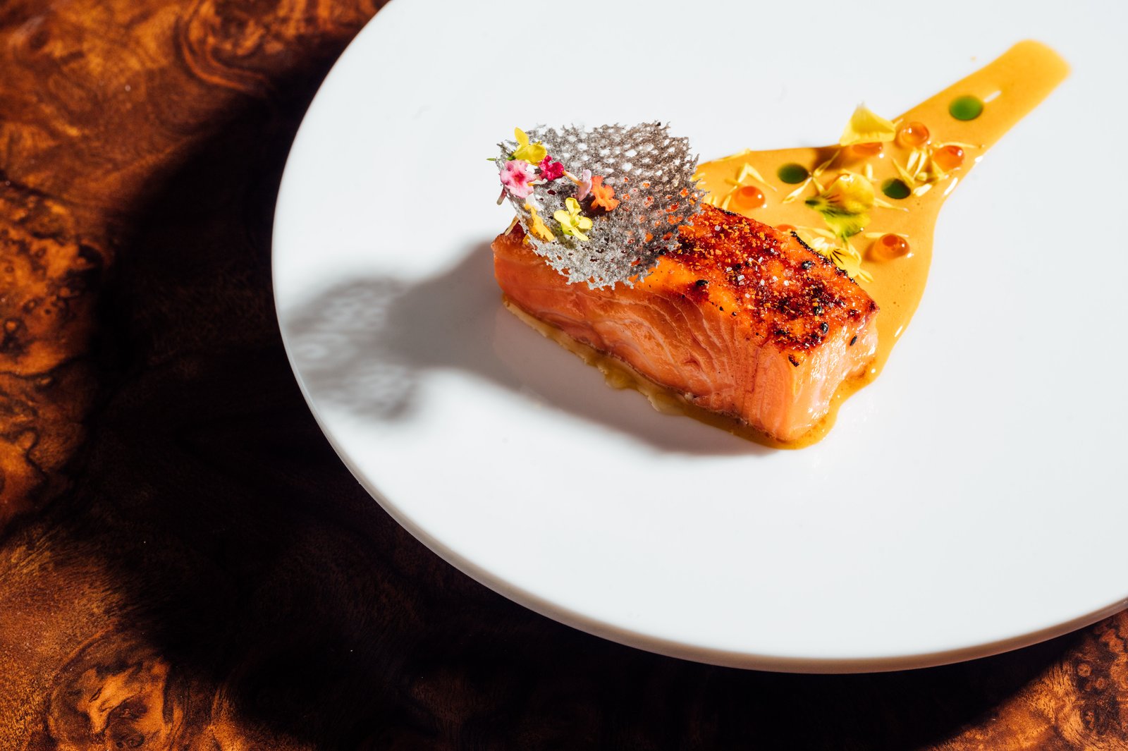 A glazed course on a white plate, finished with caviar sauce and a single edible flower.