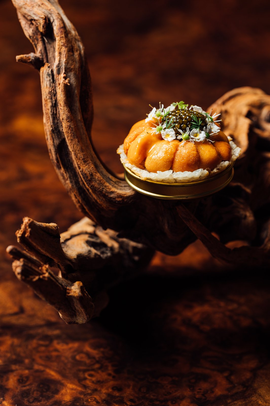 The Caviar and Uni Tart — a sunflower of custom caviar at the centre ringed by petals of creamy Hokkaido uni, presented on a gold stand on driftwood at Shin'Labo.