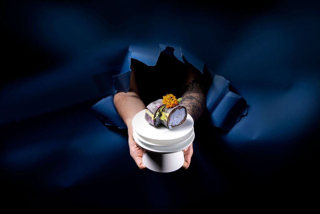 A Mortlach-marked vessel with a dish on top, served by hand through torn dark-blue paper.