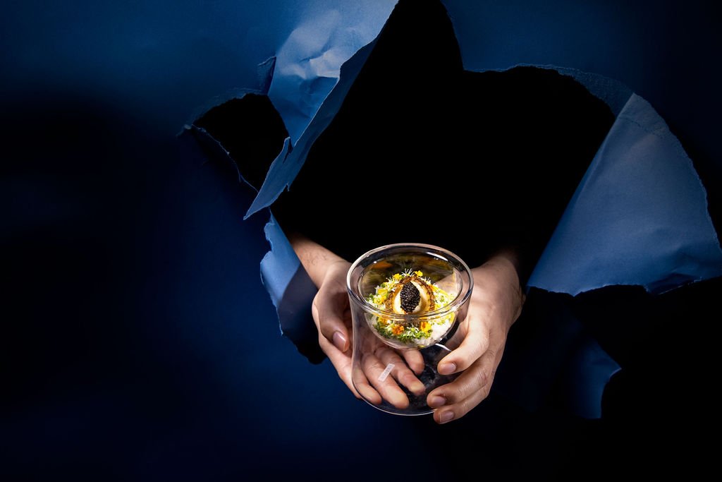A glass of Mortlach single malt held through torn dark-blue paper, the amber spirit catching the light.
