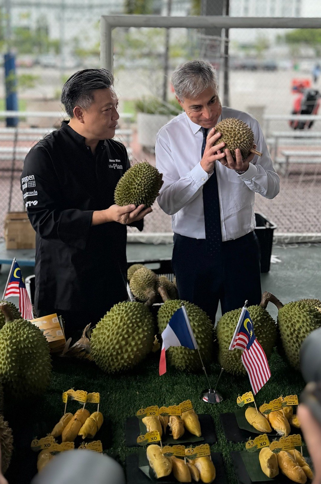 Chef James Won and His Excellency Marc Abensour examining durians, the Malaysian and French flags between them