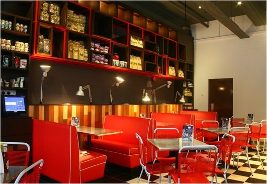 Red diner booths beneath the red pantry shelves and brass desk lamps, with a striped timber counter.
