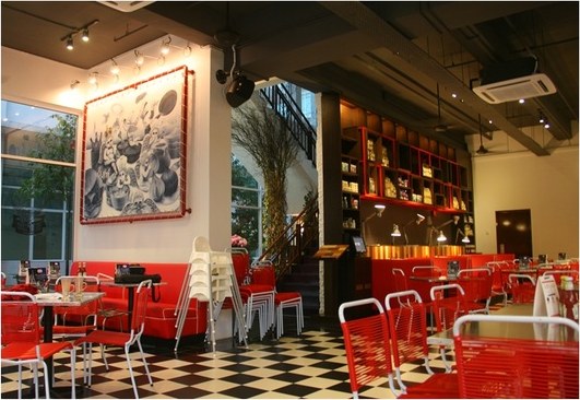 The dining room: red wire chairs, a black-and-white chequered floor and the cherub mural framed in red on the white wall.