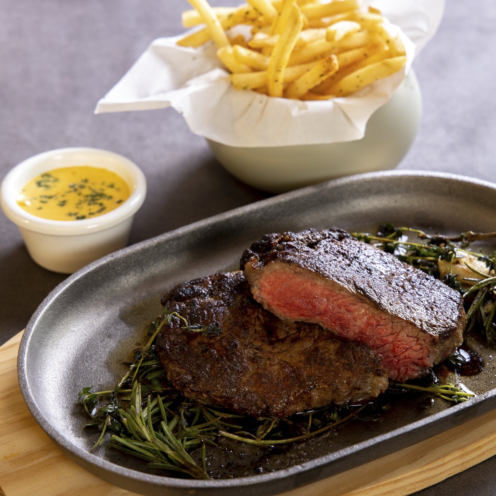 Bouchon Enfin steak frites — sliced beef on a cast-iron platter with herbs and béarnaise, frites in a paper-lined cup.