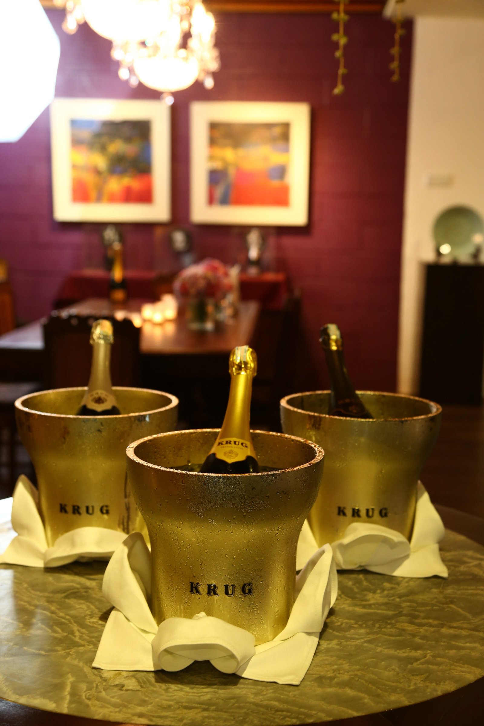 Brasserie Enfin opening night — three Krug ice buckets with bottles on the banquet table, crystal chandelier above, the burgundy room behind.