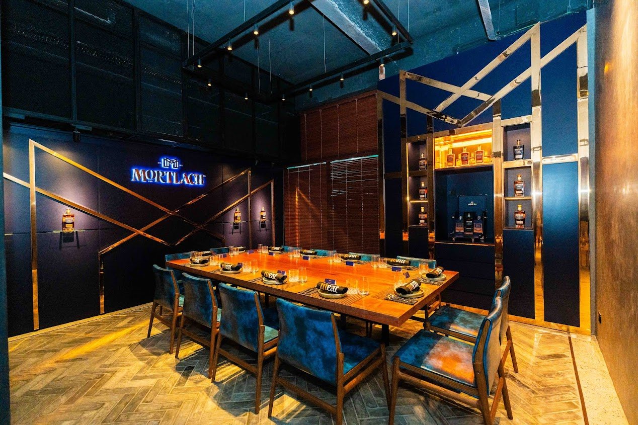 The Mortlach Room set for its launch: a long timber table under the lit Mortlach name, blue chairs on either side.