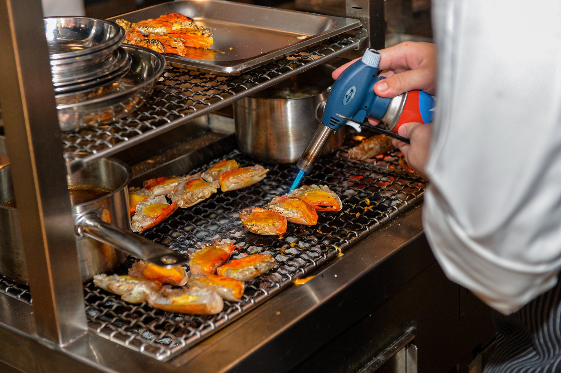 A cook torches prawns on a rack beside the grill in the Shin'Labo kitchen.