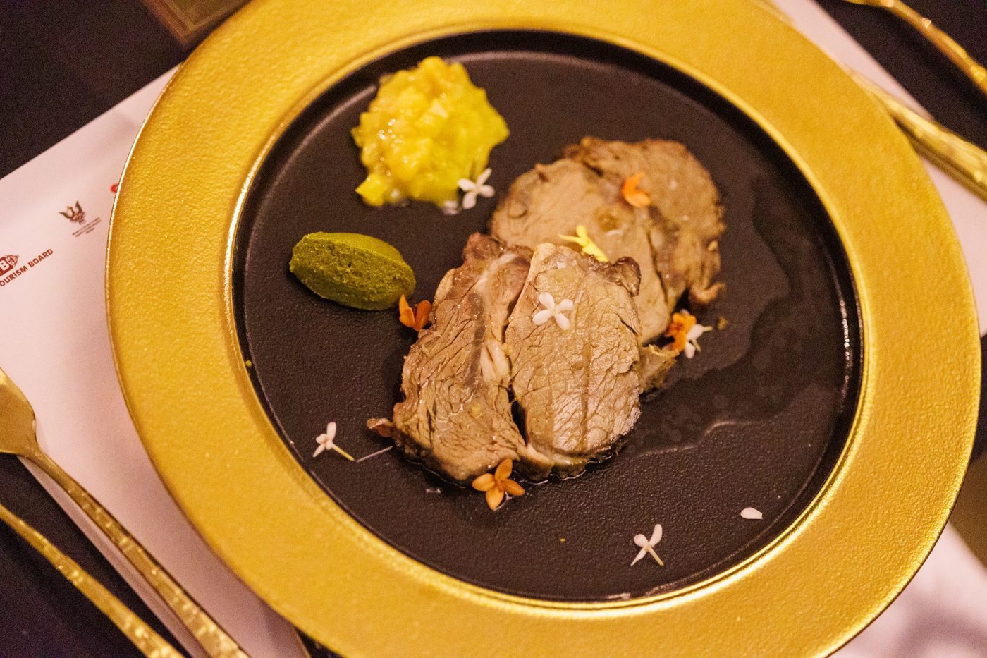 A meat course with two condiments on a gold-rimmed plate