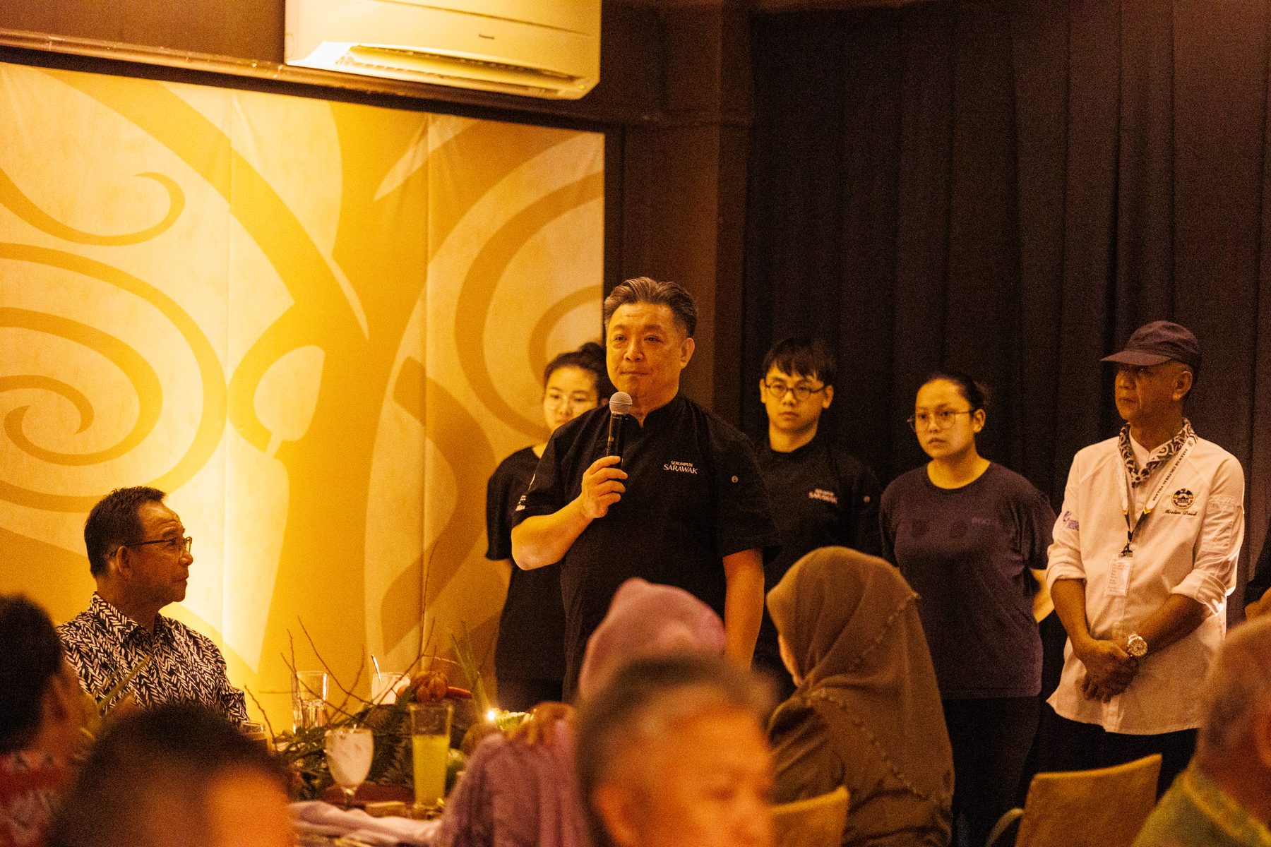 Speaking to the guests with the kitchen team standing behind